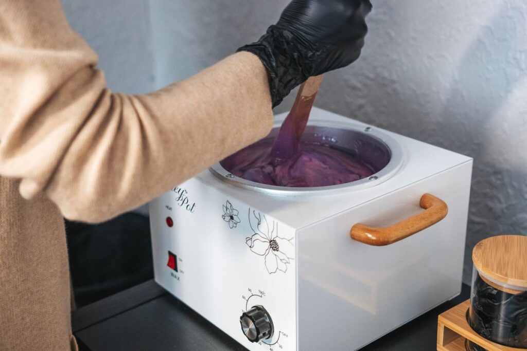 Esthetician in gloves preparing warm wax for a salon face hair removal treatment