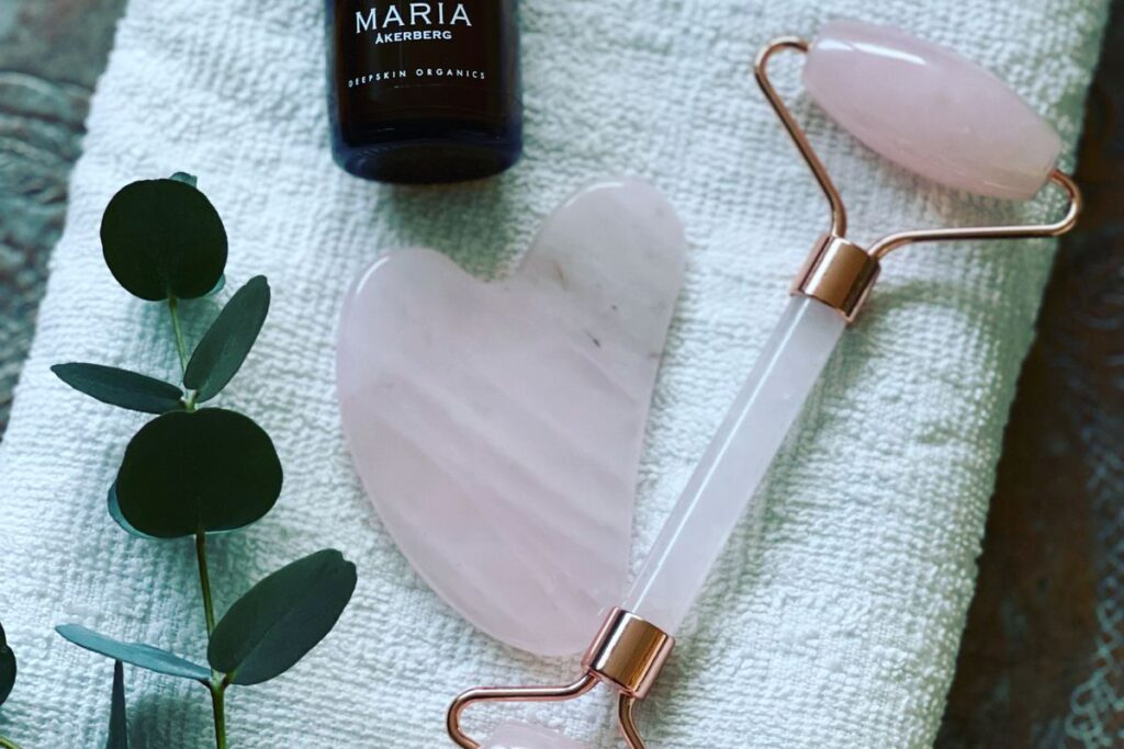 Facial roller beside a bottle of facial oil on a white towel, showing the slip needed for facial massage