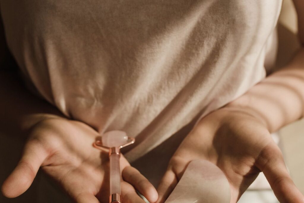 Hands holding a jade facial roller and heart-shaped gua sha stone used for facial massage